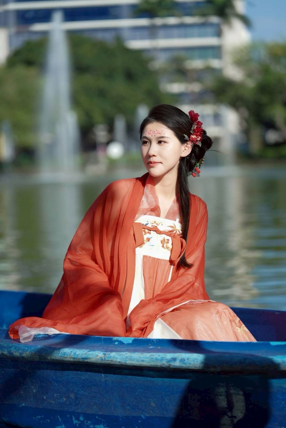 身穿朱紅齊胸襦裙、頭戴紅花盤髮的體驗者坐在湖上小舟